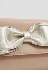 Sac à main en cuir beige avec un grand nœud métallique doré sur le rabat avant.