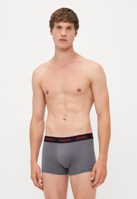 Boxers de algodón gris con una cinturilla negra que presenta el logo rojo "HUGO", diseño ajustado y textura suave.