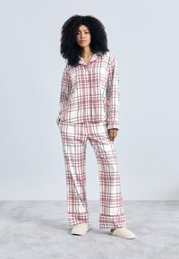 Conjunto de pijama de cuadros en beige, rojo y azul, con una camisa abotonada con cuello y pantalones de corte holgado. Tela suave con textura lisa.