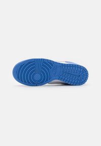 Fehér sneaker talp textúrált kék gumitalppal, körkörös és vonalas mintázattal, valamint látható márkavilágító logóval.