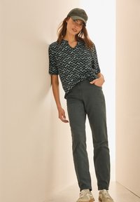 Kortärmad marinblå blus med ett zigzag-mönster, kombinerad med m�örkgröna byxor och vita sneakers. Modellen bär en grön keps.