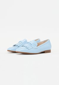 Light blue loafers with fringe detailing, made of glossy material. Flat soles with a slight brown heel. Smooth texture, simple design.