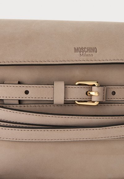 Μπεζ δερμάτινη τσάντα Moschino Milano με ραμμένη ζώνη και λεπτομέρεια με αγκράφα σε χρυσαφί τόνο στην μπροστινή πόρπη.