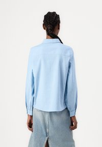Camisa de botão listrada azul clara com mangas longas e ajuste relaxado. Apresenta um colarinho clássico e punhos soltos.