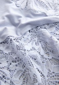 Material albastru deschis cu textură fină și detalii intricate din dantelă cu modele florale pe margine, creând un interes vizual stratificat.