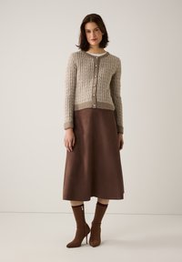 Beige knitted cardigan with textured pattern and silver buttons, paired with a brown A-line skirt and fitted brown ankle boots.