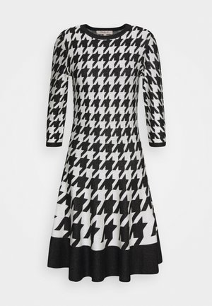 Black and white houndstooth patterned dress with three-quarter sleeves and a flared skirt with a solid black hem.