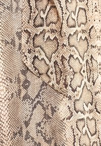 Tissu à motif peau de serpent beige et marron avec des écailles et des marques sombres symétriques, montrant la texture et des formes irrégulières naturelles.