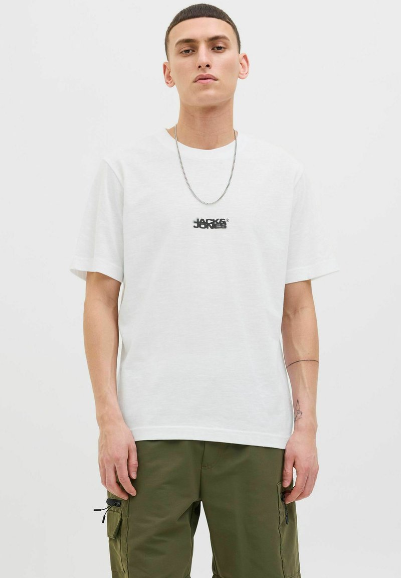 Witte katoenen T-shirt met een ronde hals en korte mouwen, voorzien van een zwart logo op de borst. Vlotte textuur, ontspannen pasvorm.