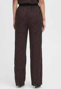 Rudos nėrinių kelnės su gėlių raštais, plačiais kojomis, aukštu liemeniu ir banguota apatine dalimi, demonstruojančios lengvą ir tekstūruotą audinį.