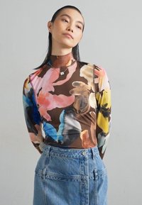 Dlhý rukáv, priliehavý top z hnedého materiálu s multicolor kvetinovou potlačou; spárovaný s džínovou sukňou s vysokým pásom a detailmi gombíkov.