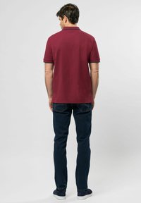 Vínový polo shirt s límečkem, kontrastní námořnické akcenty na rukávech, spárovaný s tmavě modrými džíny a námořnickými botami, pohled zezadu.
