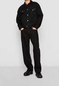 Svart denimjacka med silverknappar och två bröstfickor, matchad med svarta raka byxor och svarta läderskor.