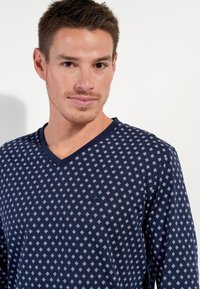 Navy patterned v-neck shirt featuring small diamond shapes in white and red. Soft fabric with a slight sheen, relaxed fit.