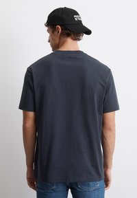 Mørk grå bomull t-skjorte med avslappet passform, korte ermer og klassisk crew-hals, kombinert med blå denimjeans og en svart caps.