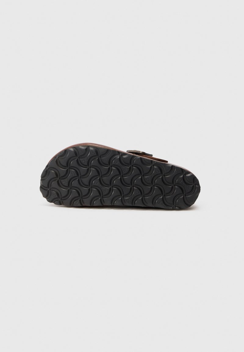 Sandal de color marrón con una suela de goma negra texturizada que presenta un patrón de olas y un detalle de hebilla central. La parte inferior se muestra de manera prominente.