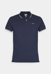 Polo bleu marine à manches courtes avec bordure blanche sur le col et les manches, deux boutons et petit logo GANT sur la poitrine gauche.