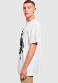 Hvid bomulds t-shirt med korte ærmer, der har et grafisk print på fronten. Pasformen er afslappet og lidt oversized.