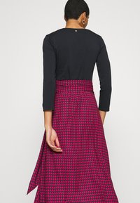 Maxikjol med svart topp. Kjolen har ett rosa och svart hundtandsmönster, hög midja och flödande tyg. Bakdetalj inkluderar en knapp.