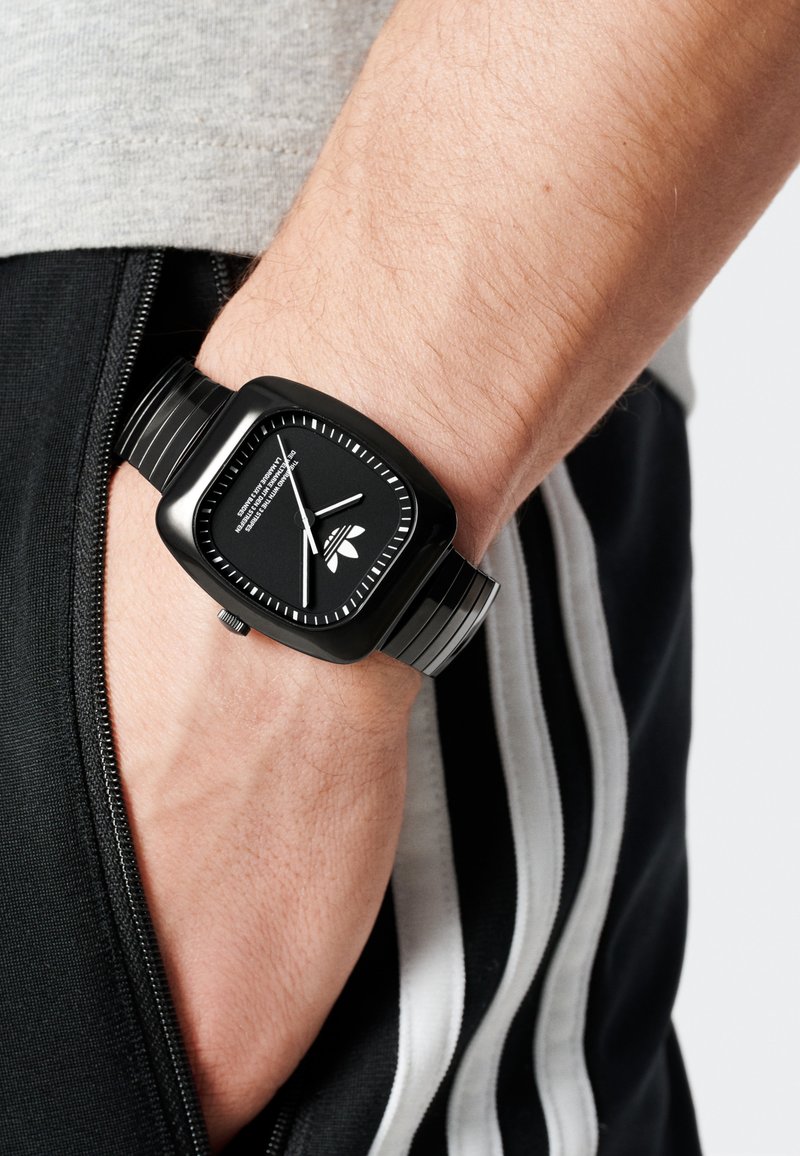 Musta ruudukujuline kell tekstureeritud silikoonpaelaga. Kellal on must sihverplaat kontrastsete valgete tunni märkidega ja logo detail.