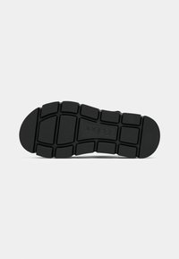 Black rubber shoe sole with a segmented pattern, featuring rectangular shapes and grooves for traction, embossed logo in the center.