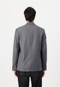 Gray pinstripe blazer made of textured fabric, featuring a vent at the back and structured shoulders, paired with black pants.