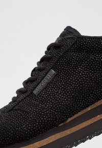 Černá teniska s texturovaným svrškem zdobeným malými kulatými nýty. Šněrovací design, gumová podrážka s vrstvenou stélkou z korku. Jemný detail s logem.