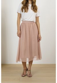 En ljusrosa, flödande, knälång kjol av genomskinligt material med elastisk midja, kombinerad med en enkel vit t-shirt och remsandaler.