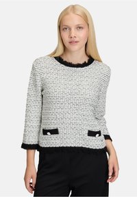 Schwarzes und weißes Tweed-Oberteil mit einem gefransten schwarzen Ausschnitt, drei Viertel langen Ärmeln und zwei schwarzen Taschen mit silbernen Knöpfen.