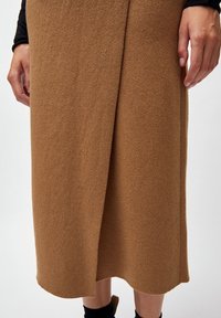 Brun, knälång kjol i mjukt, texturerat tyg med en omslagsdesign. Har en sidofåra och en slät fåll.