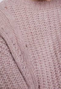 Tissu tricoté rose doux avec des motifs côtelés et torsadés et une texture légèrement duveteuse.