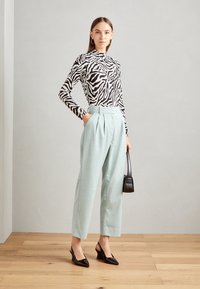 Črna in bela dolga majica z zebrastrimami ter visokim ovratnikom, v kombinaciji s svetlo modrimi širokimi hlačami z nagubanim učinkom in črnimi slingback petami.