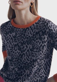 Pull avec une base grise présentant un motif léopard noir. Encolure et poignets côtelés orange contrastants. Texture douce, poids moyen.