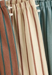 Three pairs of drawstring pants in soft, textured fabric featuring vertical stripes. Colors include brown, cream, and teal.
