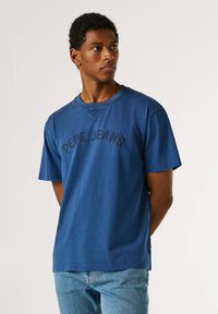 Μπλε κοντομάνικη βαμβακερή μπλούζα με στρογγυλή λαιμόκοψη και τη φράση "PEPE JEANS" τυπωμένη με μαύρα γράμματα στο στήθος.