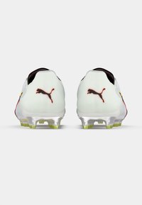 Scarpe da calcio Puma bianche con dettagli neri e una striscia gialla. Presentano una texture liscia, suola traslucida e logo prominente.