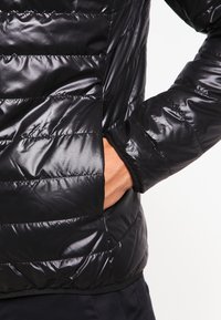 Black puffer jacket with a glossy finish, featuring quilted texture, side pockets, and elastic cuffs for added comfort and fit.