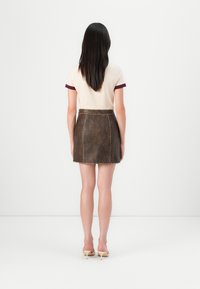 Brun kunstskinn mini skjørt med en glatt tekstur, baklås og synlige sømdetaljer. Båret med en lys topp med burgunder detaljer.