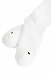 Chaussettes blanches en tissu lisse, avec une texture côtelée. Étiquettes noires "G" et "D" brodées sur les orteils pour identifier le pied gauche et le pied droit.