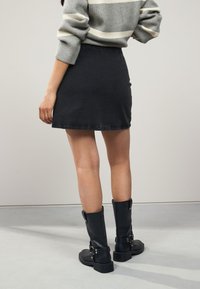 Black denim mini skirt with a straight shape, featuring a classic hem and rear pockets, paired with tall black leather boots with buckles.