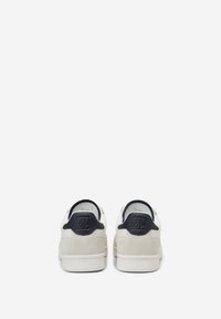 Paire de baskets basses blanches avec languettes de talon noires et logo embossé, vues de dos sur fond blanc uni.