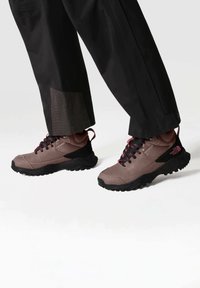 Scarpe da trekking marroni con dettagli neri e lacci rosa. Caratterizzate da una suola testurizzata e un corpo imbottito per supporto e aderenza.