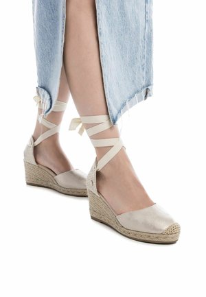 Cuñas de espadrilles en beige con suela de yute trenzado, parte superior de satén y cintas en el tobillo. Presentan puntera cerrada y tacón plano.