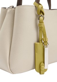 Beżowa torebka skórzana o teksturowanej powierzchni z brązowymi uchwytami oraz żółtym skórzanym znaczkiem na pasku, ozdobiona srebrnym prostokątnym zawieszką.