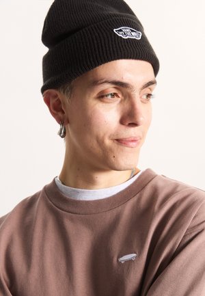 Schwarze gerippte Mütze mit gesticktem Logo, kombiniert mit einem braunen Sweatshirt, das ein kleines Skateboard-Graphic auf der Brust zeigt. Lässiger Stil.
