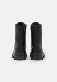 Botas de tobillo de cuero negro con una textura suave, cierre con cremallera y suelas de goma. Presentan un logo grabado en el talón.