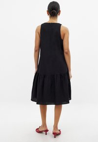 Musta hihaton mekko, jossa on teksturoidun pinnan, levenevä röyhelöhelma ja takana suljenta. Yhdistetty punaisiin korkokenkiin.