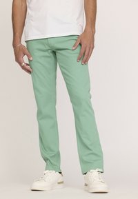 Pantalons droits vert menthe en coton avec une texture lisse, associés à des baskets blanches avec des accents dorés.