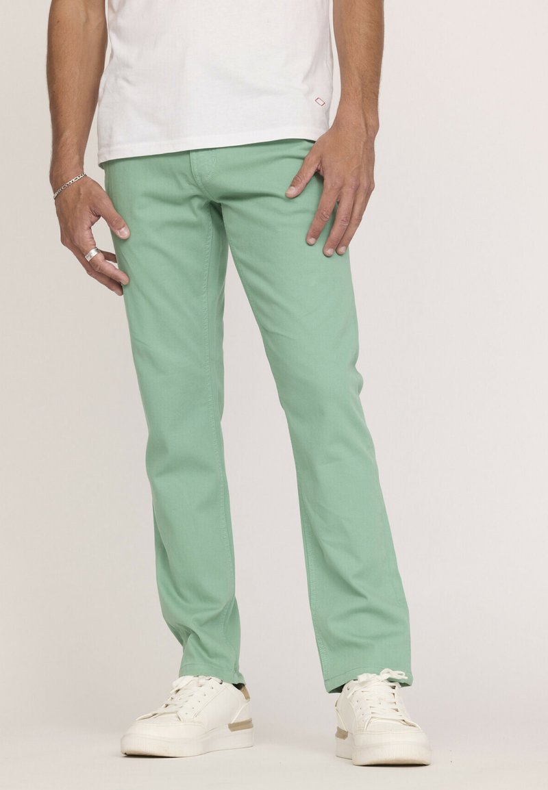 Pantalons droits vert menthe en coton avec une texture lisse, associés à des baskets blanches avec des accents dorés.
