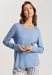 Camisa de cuello redondo de manga larga azul claro, fabricada en un tejido suave, con un corte holgado y detalles de costura sutiles. Combinada con pantalones a rayas.